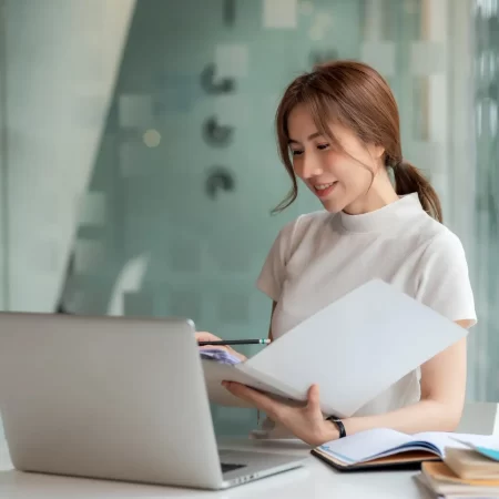 Beautiful Young Asian businesswoman holding documents to checking authenticity the laptop is placed